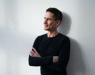 Business Software Berater in schwarzem Pullover mit verschränkten Armen vor hellem Hintergrund in professioneller Seitenansicht.