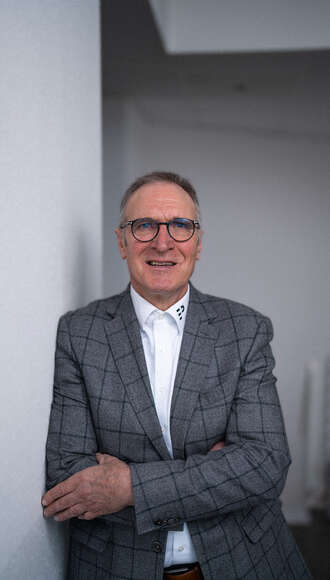 Business Software Spezialist mit Brille in grauem Sakko und weißem Hemd, freundlich lächelnd in professioneller Pose vor hellem Büro-Hintergrund.